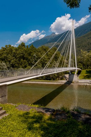 Photo for Modern pedestrian bridge in the middle of the mountains of Italian Switzerland, which allows you to cross the Ticino river. Beautiful sunny summer day. - Royalty Free Image