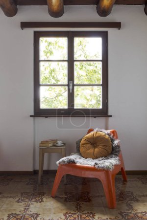 Photo for A window and below it a small orange armchair with a stool that serves as a table. Detail of furniture. Old-style holiday home - Royalty Free Image