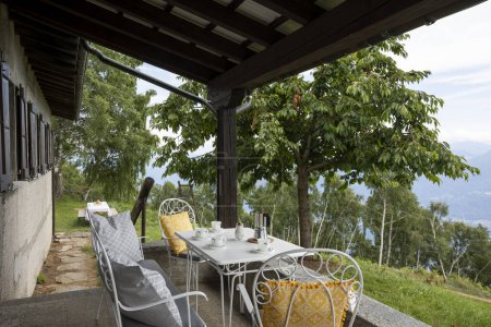Foto de Terraza con muebles antiguos y una vista de la naturaleza. hay sillas un banco y un juego de mesa para tomar un café. Suiza - Imagen libre de derechos