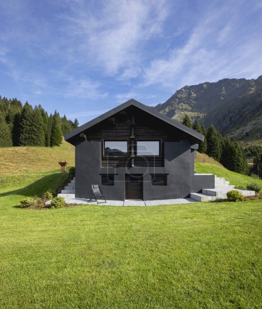 Téléchargez les photos : Un chalet de montagne suisse très insolite car il est noir et en bois. Entouré d'une belle prairie verte d'été. Le ciel est bleu et il ressemble à un endroit calme et très paisible. - en image libre de droit