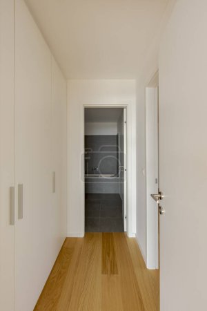 Téléchargez les photos : Vue de face d'un couloir avec un dressing sur le côté et à l'extrémité, la porte ouverte menant à la salle de bain. Parquet. Personne à l'intérieur. - en image libre de droit