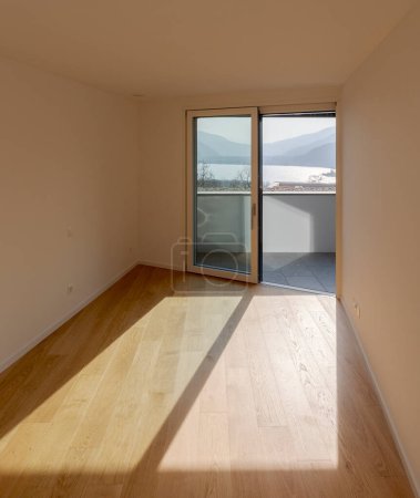 Téléchargez les photos : L'intérieur d'un appartement moderne avec du parquet. La lumière du soleil coule à travers la fenêtre offrant une vue pittoresque sur les montagnes et le lac de Suisse. Personne présent. - en image libre de droit