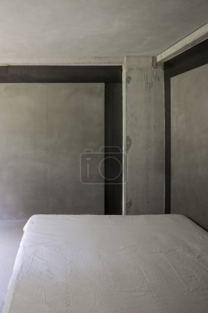 Téléchargez les photos : Une vue d'un lit avec des couvertures blanches, situé dans un environnement de murs en béton rugueux. Il n'y a personne dedans.. - en image libre de droit