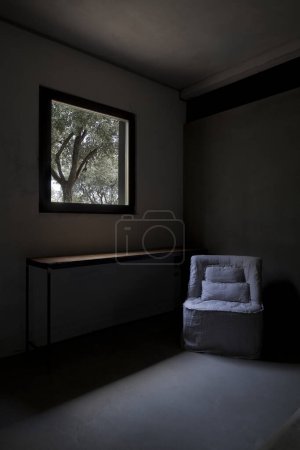 Téléchargez les photos : Détail d'une chaise confortable avec un coussin dessus. La lumière du soleil brille à travers la fenêtre, avec vue sur les oliviers. Il n'y a personne dedans.. - en image libre de droit