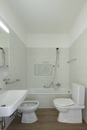 Téléchargez les photos : Intérieur d'une salle de bain dans un appartement normal, ni pauvre ni riche. Tout est blanc et il n'y a personne à l'intérieur. Le sol est en bois - en image libre de droit