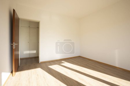 Téléchargez les photos : Chambre vide avec des murs blancs, une porte ouverte où vous pouvez voir le couloir avec des armoires intégrées. Personne à l'intérieur - en image libre de droit