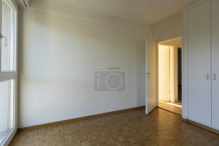 Photo for Empty room with white walls, parquet floor and a closed closet. Open door overlooking the hallway. No one inside. - Royalty Free Image