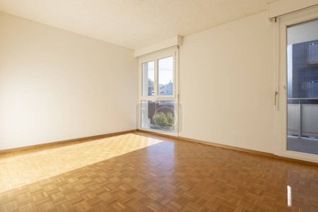 Téléchargez les photos : Chambre vide avec murs blancs et parquet. Il y a une fenêtre donnant sur la nature. Personne à l'intérieur - en image libre de droit