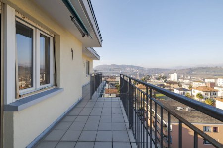 Foto de Vista desde una terraza de un apartamento en el último piso. Se puede ver la ciudad de abajo y las montañas en la distancia. Día de invierno soleado - Imagen libre de derechos