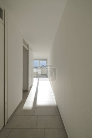 Téléchargez les photos : Vue de face d'un couloir avec la porte ouverte et le soleil entrant et créant une ombre très longue sur le sol. Personne à l'intérieur - en image libre de droit
