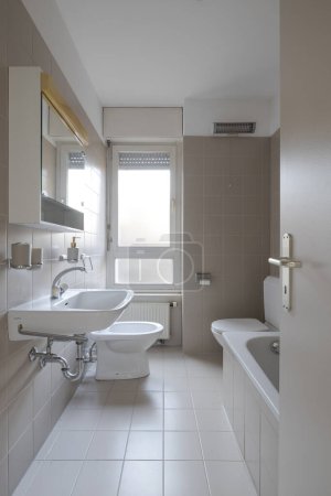 Téléchargez les photos : Vue de face d'une ancienne salle de bain avec des carreaux et une fenêtre lumineuse. Il y a aussi une baignoire. Personne à l'intérieur - en image libre de droit