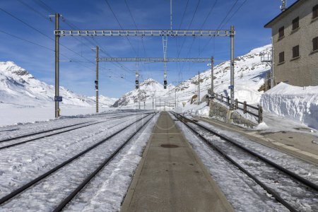 Train station on the Bernina Pass in Switzerland. Front view from the railway platform and tracks appearing from the snow. Nobody inside