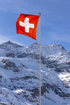 Detail of the Swiss flag waving very strongly due to the strong wind. In the background the snow-capped mountain. Nobody inside