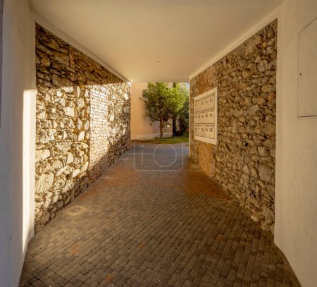 Photo for Entrance hall of a renovated courtyard house. There are rough rocks on the walls, mailboxes on the right, and a green tree at the bottom. No one inside - Royalty Free Image