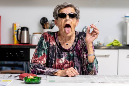 Photo for Woman sitting at the table with a cigarette in her hand while grimacing - Royalty Free Image