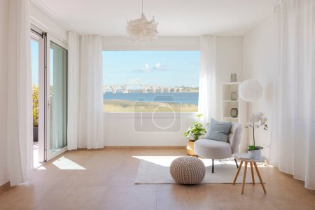 Photo for Front view of a living room corner with a small armchair and a coffee table. There is a large window from which you can admire an impressive bridge spanning a large river. Nobody inside - Royalty Free Image