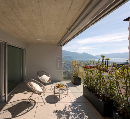 Large terrace in Switzerland with comfortable chairs and cushions and a small table. it's a sunny day and the view is spectacular, you can see the lake and the mountains. 