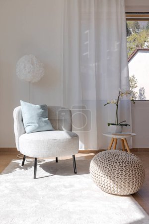 Foto de Detalle de un rincón de la sala de estar con un pequeño sillón con una mesa de centro y un puf que descansa sobre la alfombra. Nadie dentro. - Imagen libre de derechos