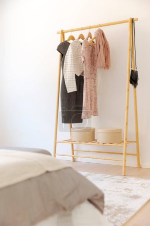 Photo for Detail of a wooden rella with elegant women's clothes hanging from it. In the foreground you can see part of the bed with blankets. No one inside - Royalty Free Image