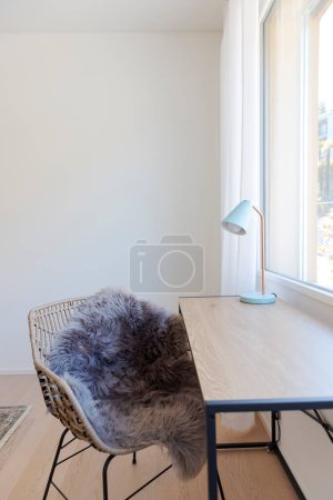 Foto de Detalle de un pequeño escritorio de madera con un sillón y una bombilla. Hay una ventana brillante que ilumina la escena. - Imagen libre de derechos