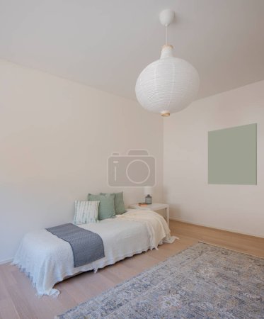 Photo for Detail of a single bedroom with a bed covered with blankets and many pillows. There is a nice carpet on the floor and space for a painting on the side. No one inside. - Royalty Free Image