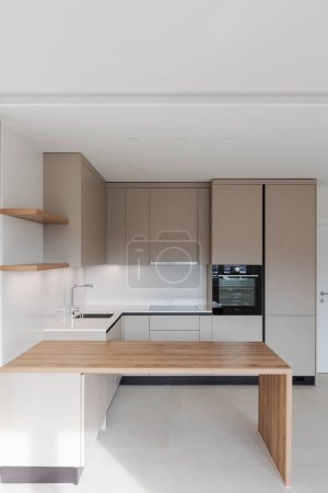Foto de Vista frontal de una nueva cocina con una robusta mesa de madera en frente. - Imagen libre de derechos