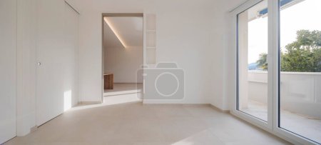 Photo for Empty space sconces an open sliding door in the background. On the ceiling there is a lighted LED and to the right a large window leading onto the balcony. It is a vuotom and modern, new flat. - Royalty Free Image