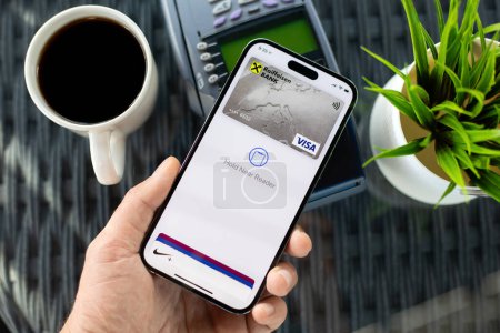 Téléchargez les photos : Alanya, Turquie - Décembre 1, 2023 : Homme main tenant iPhone 15 Pro Max avec app Apple Pay Raiffeisenbank sur l'écran et payer passer en ligne terminal POS acheter le café dans le café. - en image libre de droit