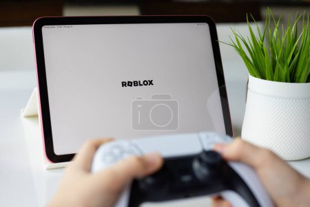 Photo for Alanya, Turkey - April 11, 2024: Children hands holding DualSense wireless controller PlayStation 5 and Apple iPad Air with multiplayer online game Roblox mobile in the screen IOS tablet - Royalty Free Image