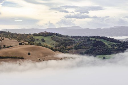 Foto de Niebla de la mañana y nubes sobre las colinas de Montefeltro cerca de Belvedere Fogliense entre Pesaro y Urbino en la región de las Marcas de Italia. El pueblo de Montefabbri aparece en el fondo. - Imagen libre de derechos