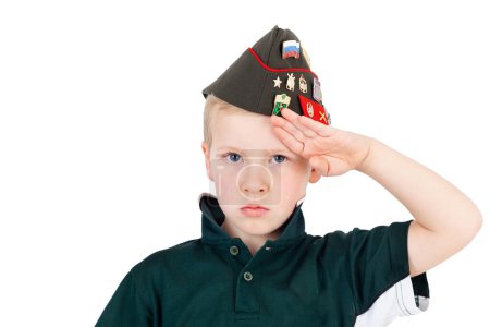 Téléchargez les photos : Jeune garçon caucasien saluant les robes de jeu en chemise verte "armée" et chapeau de l'armée russe pliante pilotka de l'armée rouge soviétique avec des épinglettes, des insignes recréés à partir de surplus d'origine de la Russie vintage - en image libre de droit