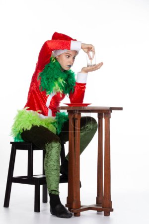 Foto de Retrato completo de una chica joven que usa un sombrero rojo de Santa Claus como el look de pregunta de Grinch con leche vacía, aislada sobre un fondo blanco. Emoción humana expresión facial - Imagen libre de derechos