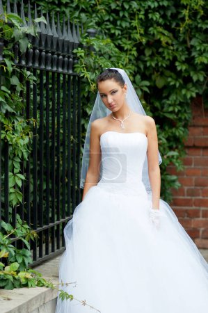 Foto de Mujer, novia en vestido de novia blanco se encuentra cerca de cerca de hierro, follaje verde - Imagen libre de derechos