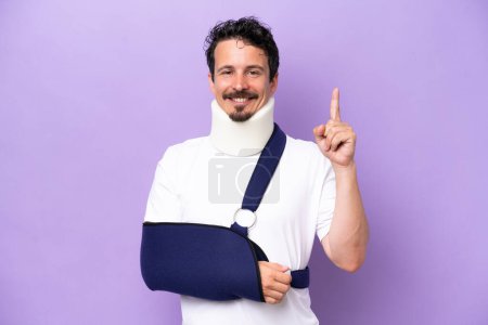 Photo for Young caucasian man wearing a sling and neck brace isolated on purple background pointing up a great idea - Royalty Free Image