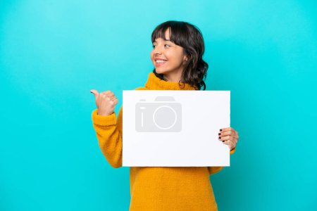 Photo for Young latin woman isolated on blue background holding an empty placard and pointing side - Royalty Free Image