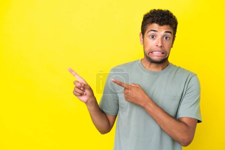 Téléchargez les photos : Jeune bel homme brésilien isolé sur fond jaune effrayé et pointant vers le côté - en image libre de droit