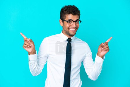 Foto de Joven hombre brasileño de negocios aislado sobre fondo azul señalando el dedo a los laterales y feliz - Imagen libre de derechos