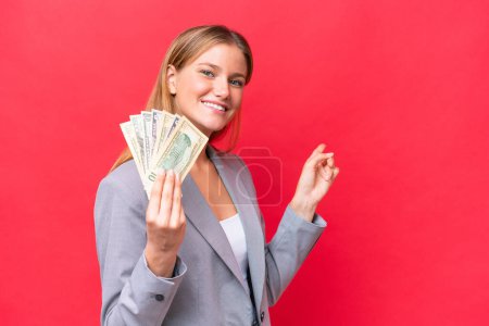 Téléchargez les photos : Jeune entreprise caucasienne femme tenant de l'argent isolé sur fond rouge pointant vers l'arrière - en image libre de droit