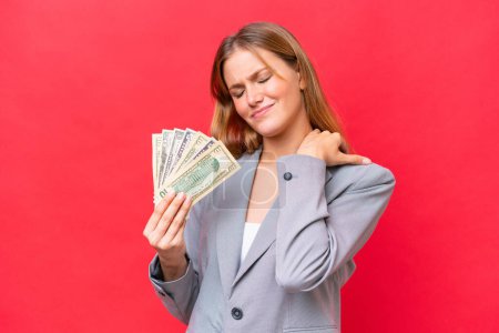 Junge unternehmerische Kaukasierin mit Geld auf rotem Hintergrund, die unter Schulterschmerzen leidet, weil sie sich bemüht hat