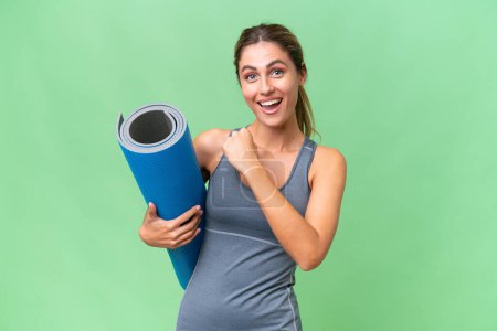 Pretty Young Uruguayan sport woman going to yoga classes while holding a mat over isolated background celebrating a victory