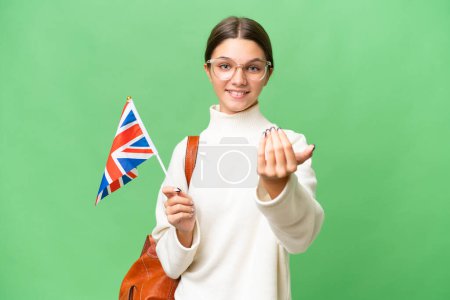 Téléchargez les photos : Adolescente étudiante caucasienne tenant un drapeau du Royaume-Uni sur fond isolé invitant à venir avec la main. Heureux que tu sois venu - en image libre de droit