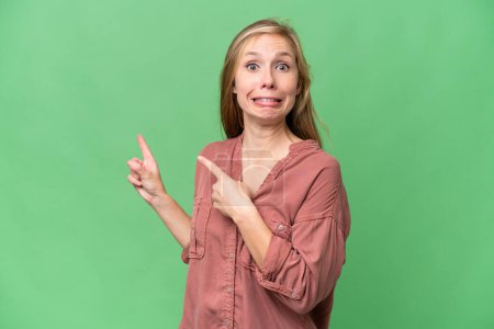 Photo for Young blonde woman over isolated background frightened and pointing to the side - Royalty Free Image