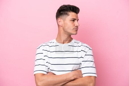 Young caucasian man isolated on pink background keeping the arms crossed