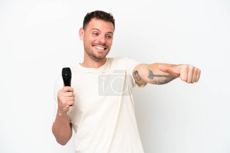 Photo pour Jeune chanteur caucasien homme ramasser un microphone isolé sur fond blanc donnant un pouce geste - image libre de droit
