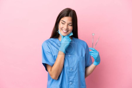 Photo for Dentist woman holding tools isolated on pink background looking to the side and smiling - Royalty Free Image