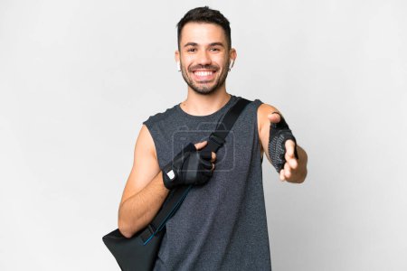 Foto de Young sport caucasian man with sport bag over over isolated white background shaking hands for closing a good deal - Imagen libre de derechos