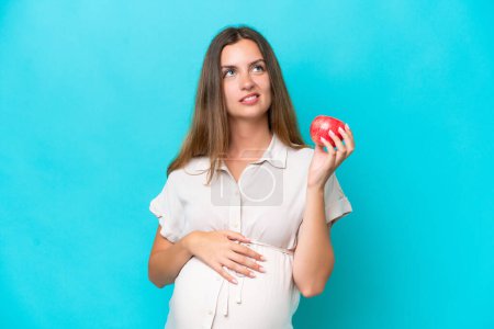 Photo for Young caucasian woman isolated on blue background pregnant and frustrated while holding an apple - Royalty Free Image