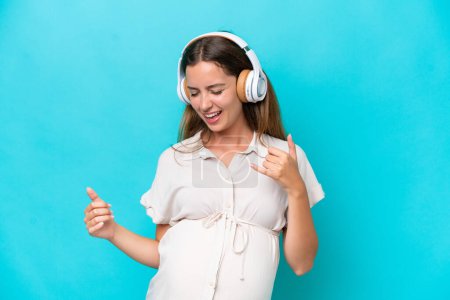 Foto de Young caucasian woman isolated on blue background pregnant and listening music - Imagen libre de derechos
