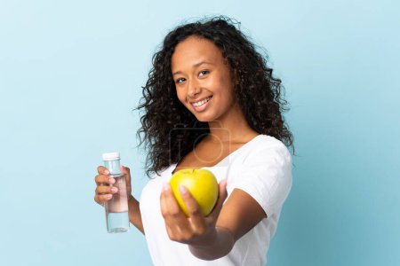 Photo for Teenager cuban girl isolated on blue background with an apple and with a bottle of water - Royalty Free Image