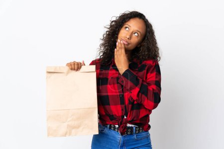 Photo for Teenager girl holding a grocery shopping bag to takeaway isolated on white background looking up while smiling - Royalty Free Image
